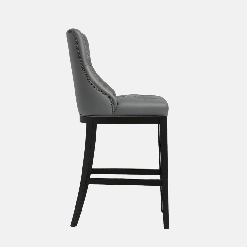 Elegant bar stool with tufted grey leather upholstered backrest and seat, black wooden legs, and metal footrest.