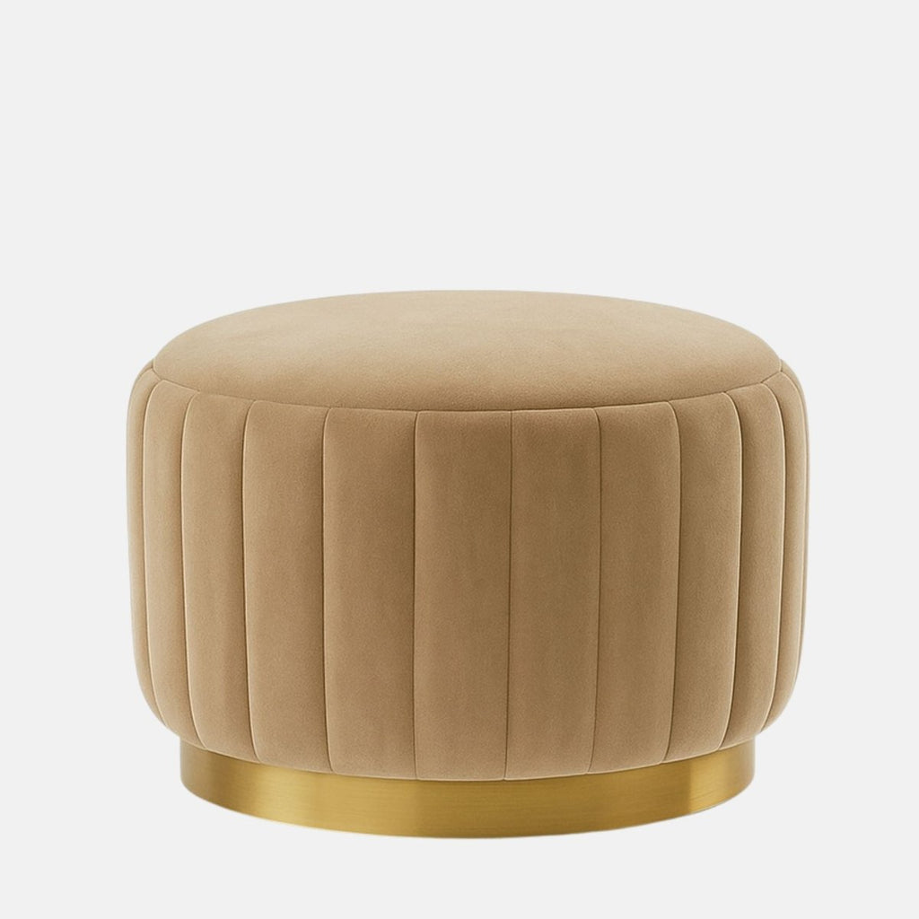 Beige velvet round ottoman with vertical panel design and brushed brass base modern upholstered stool or coffee table for living room, bedroom, or hotel lounge.
