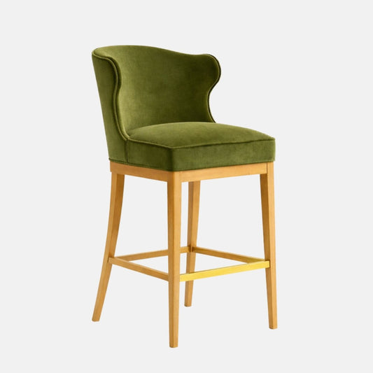 Olive green velvet bar stool with a softly curved wraparound back and thick cushioned seat, on a light oak wooden frame with square stretchers and a brass front footrest, photographed on a white background.