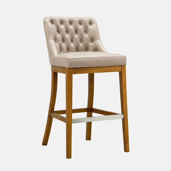 Beige upholstered bar stool with a button-tufted backrest, smooth cushioned seat, and tapered wooden legs with a metal footrest bar.