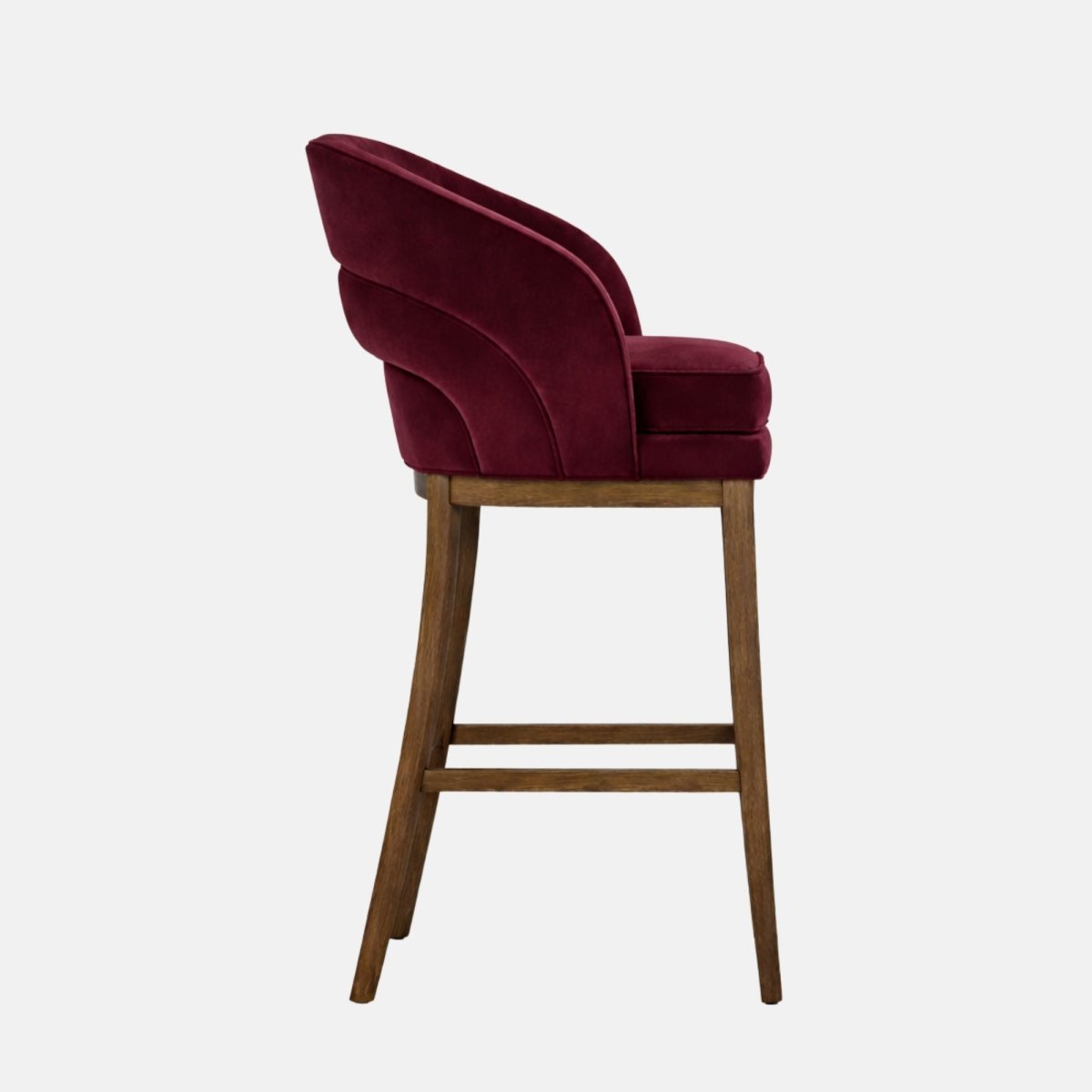 Side view of a burgundy velvet bar stool with a curved wraparound back and thick cushioned seat, on dark wooden legs with square stretchers, photographed on a white background.
