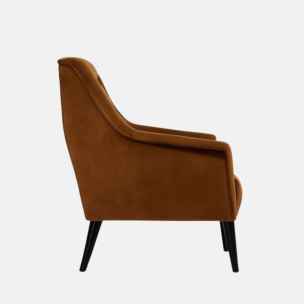 Mid-century style armchair with warm brown velvet upholstery, angled arms, a smooth backrest, and slim black tapered legs.