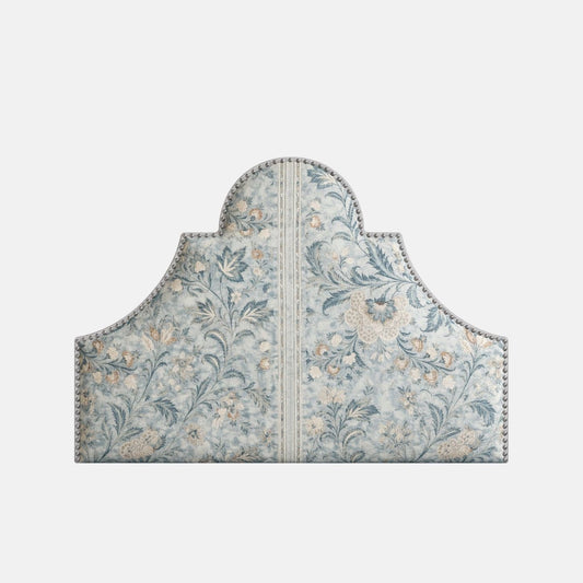 Upholstered headboard with a scalloped silhouette, blue floral pattern, and decorative nailhead trim, shown on a neutral background.