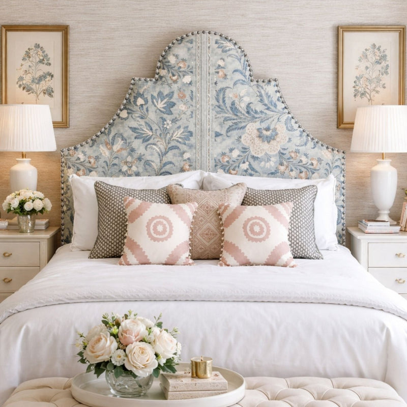 Elegant bedroom with a blue floral upholstered headboard, white bedding, and soft decorative pillows, styled with matching bedside tables and classic lighting.