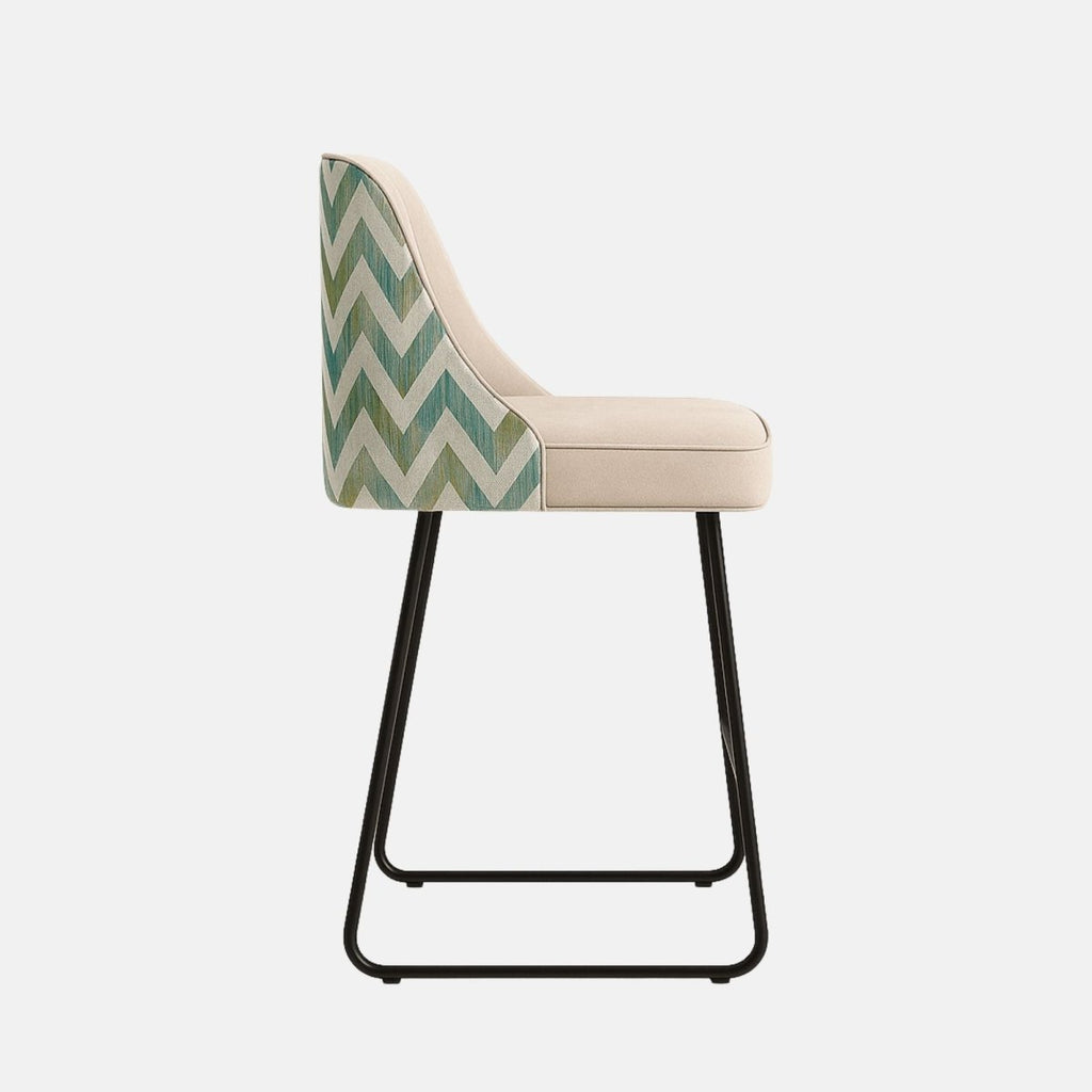 A modern bar stool featuring a cream velvet upholstered seat with vertical stitching, complemented by a chevron-patterned fabric on the backrest sides and supported by sleek black metal legs.