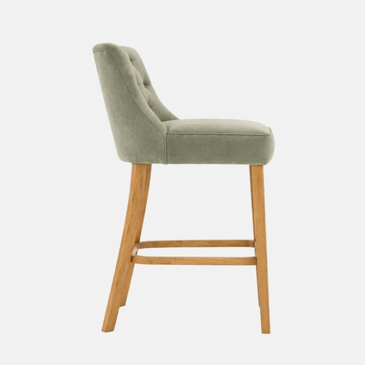 Green upholstered bar stool with button tufted backrest and wooden legs, side view