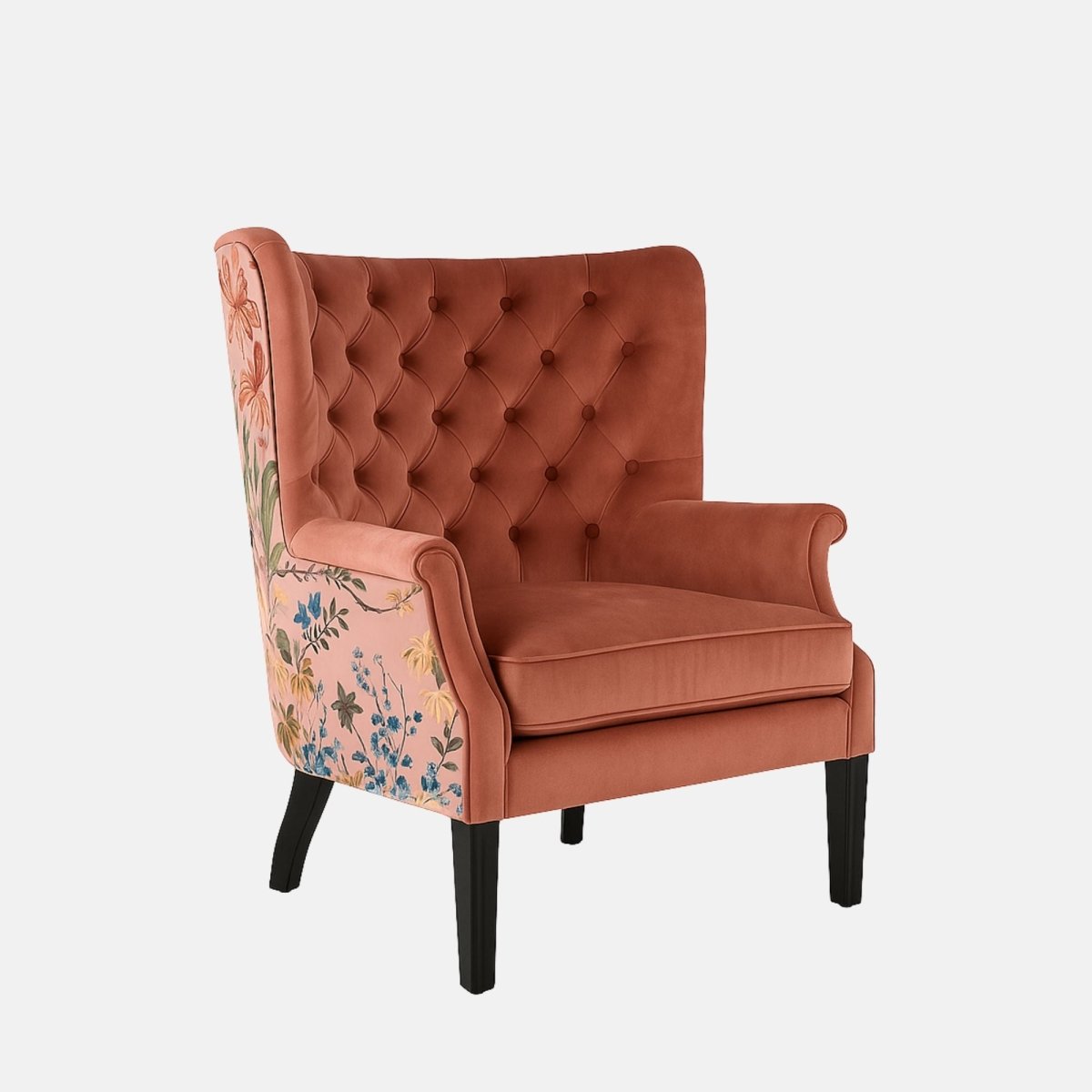 Coral-pink tufted wingback armchair with rolled arms, black legs, and floral patterned fabric on the outer back and sides.