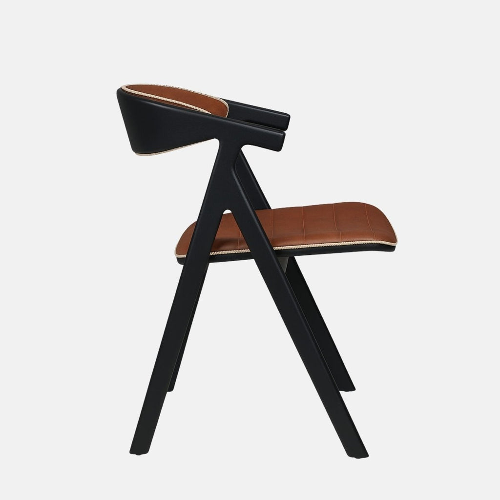 Contemporary dining chair with a black wooden frame and angled legs, featuring brown leather upholstery on the seat and curved backrest with light trim detailing, set against a light grey background.