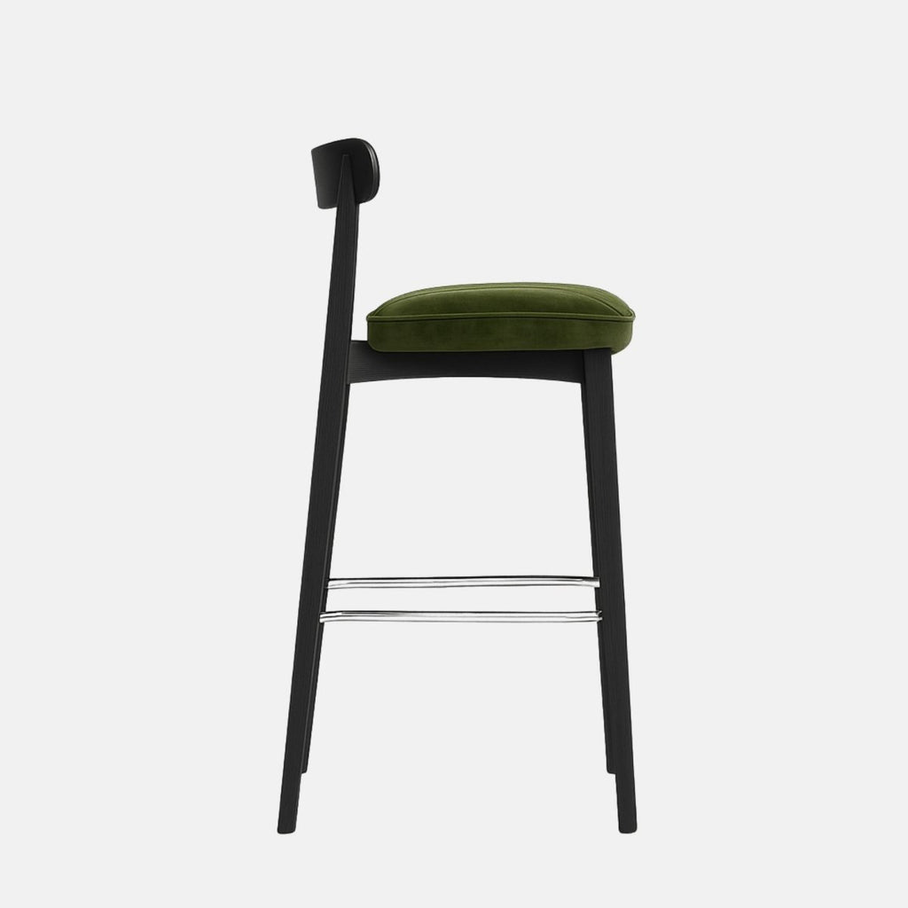 Contemporary bar stool with a black wooden frame, curved backrest, and olive green velvet seat featuring horizontal channel stitching and a metal footrest.
