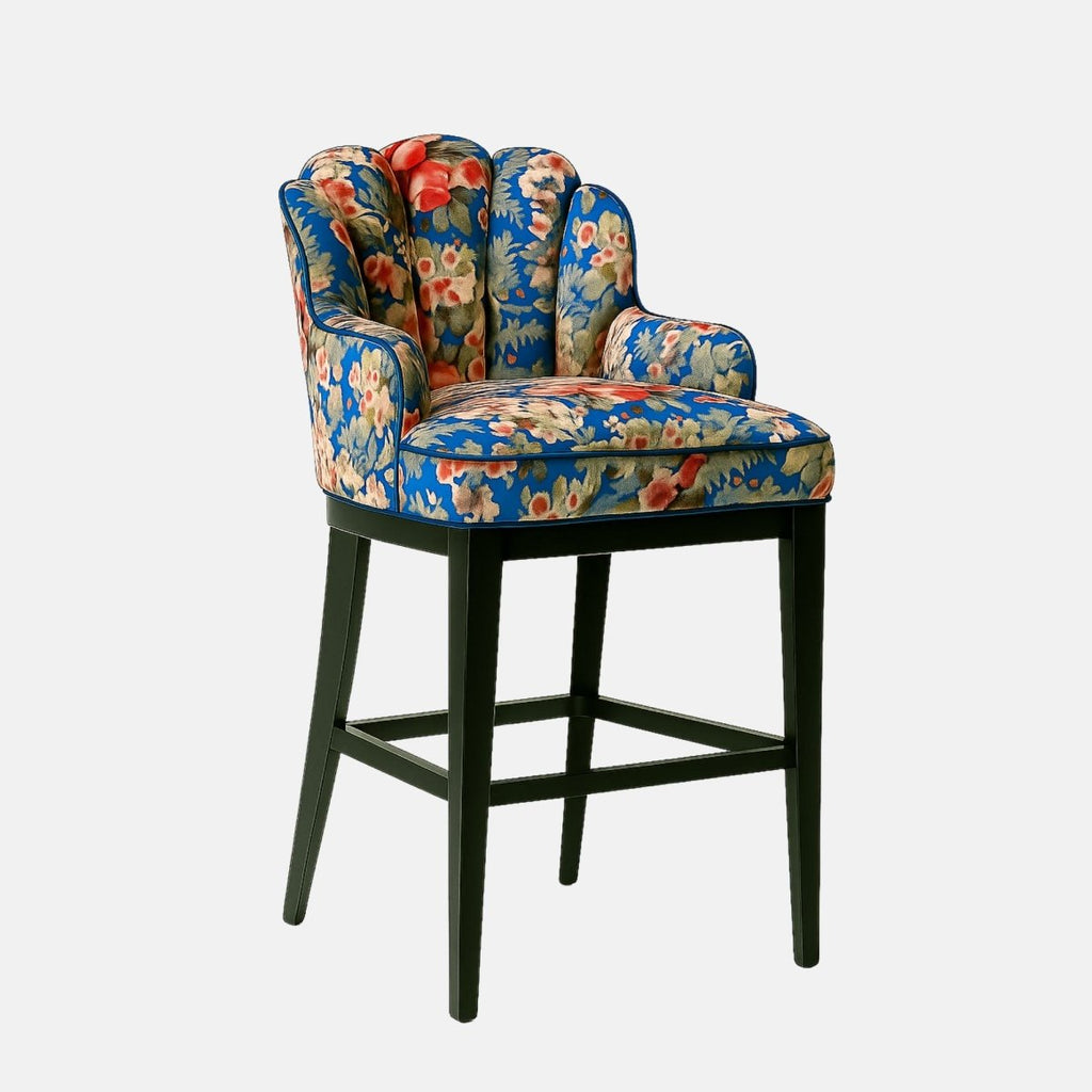 Elegant bar stool with a scalloped backrest and arm design, upholstered in a vibrant blue floral fabric featuring red, cream, and green tones. The seat is plush and supported by a sleek black wooden frame, blending vintage charm with modern sophistication.