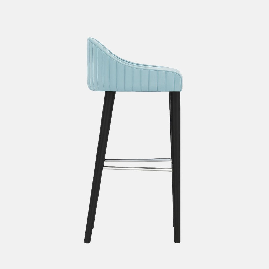 Contemporary bar stool with light blue upholstered seat and back featuring vertical channel stitching, black tapered legs, and a metal footrest.