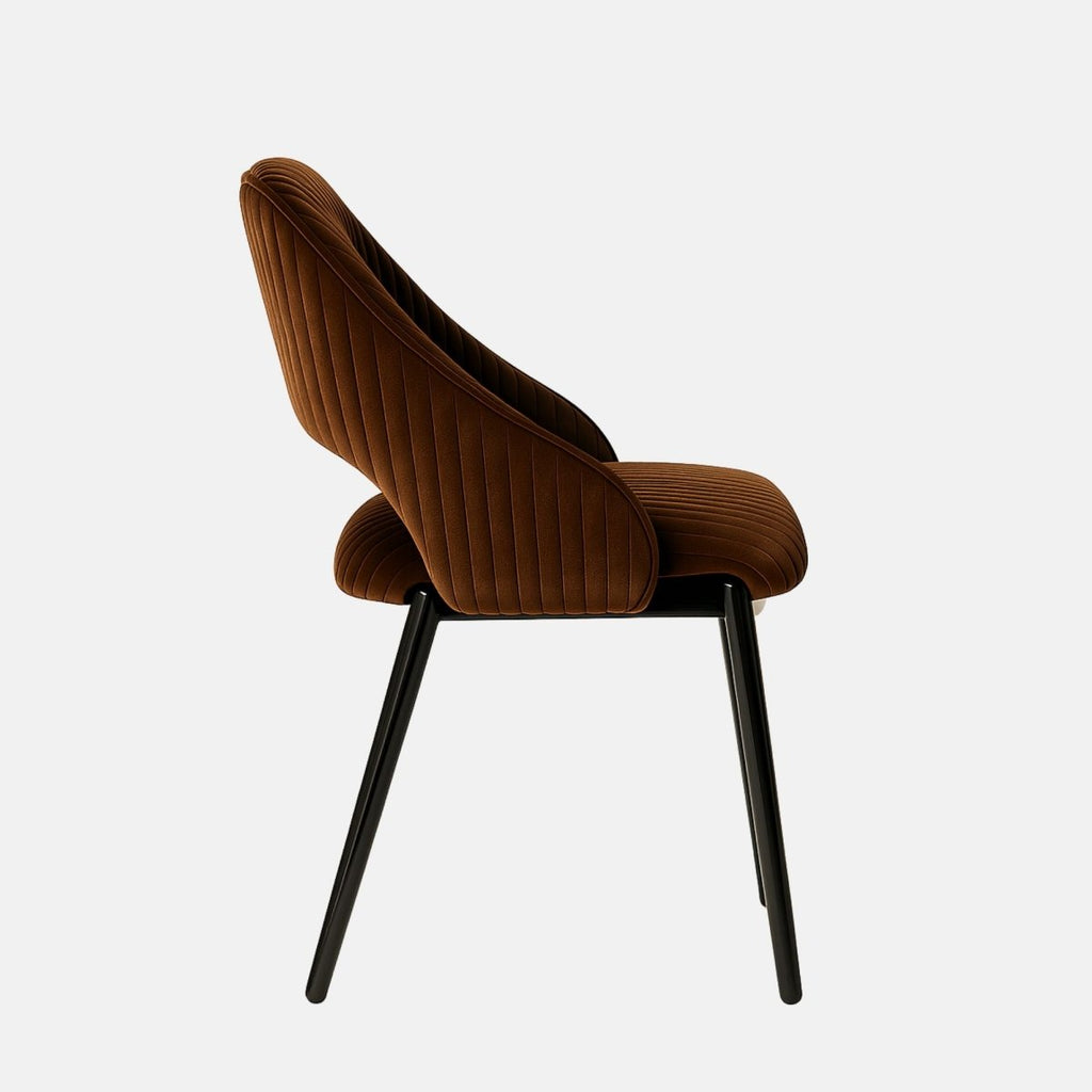 Contemporary dining chair with black metal legs and a curved backrest, upholstered in rich brown velvet with vertical channel stitching and an open lower back design, set against a light grey background