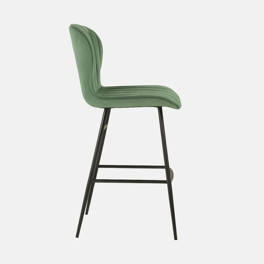 Modern green velvet bar stool with high curved backrest, vertical channel tufting, and slim black metal legs with footrest.