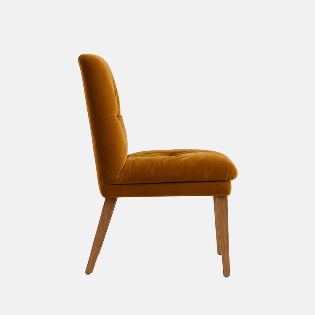 Upholstered dining chair in warm mustard velvet with a softly ruched cushioned seat and backrest, supported by tapered wooden legs, shown on a white background