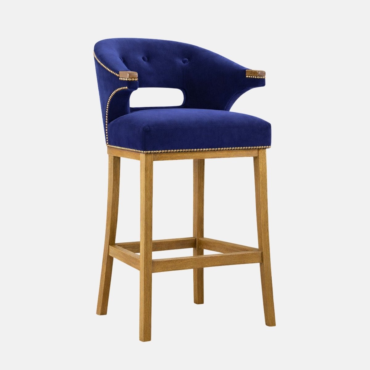 Navy velvet bar stool with a curved wraparound back and side cutout, button detailing, nailhead trim, and light wood legs with a square stretcher/footrest.