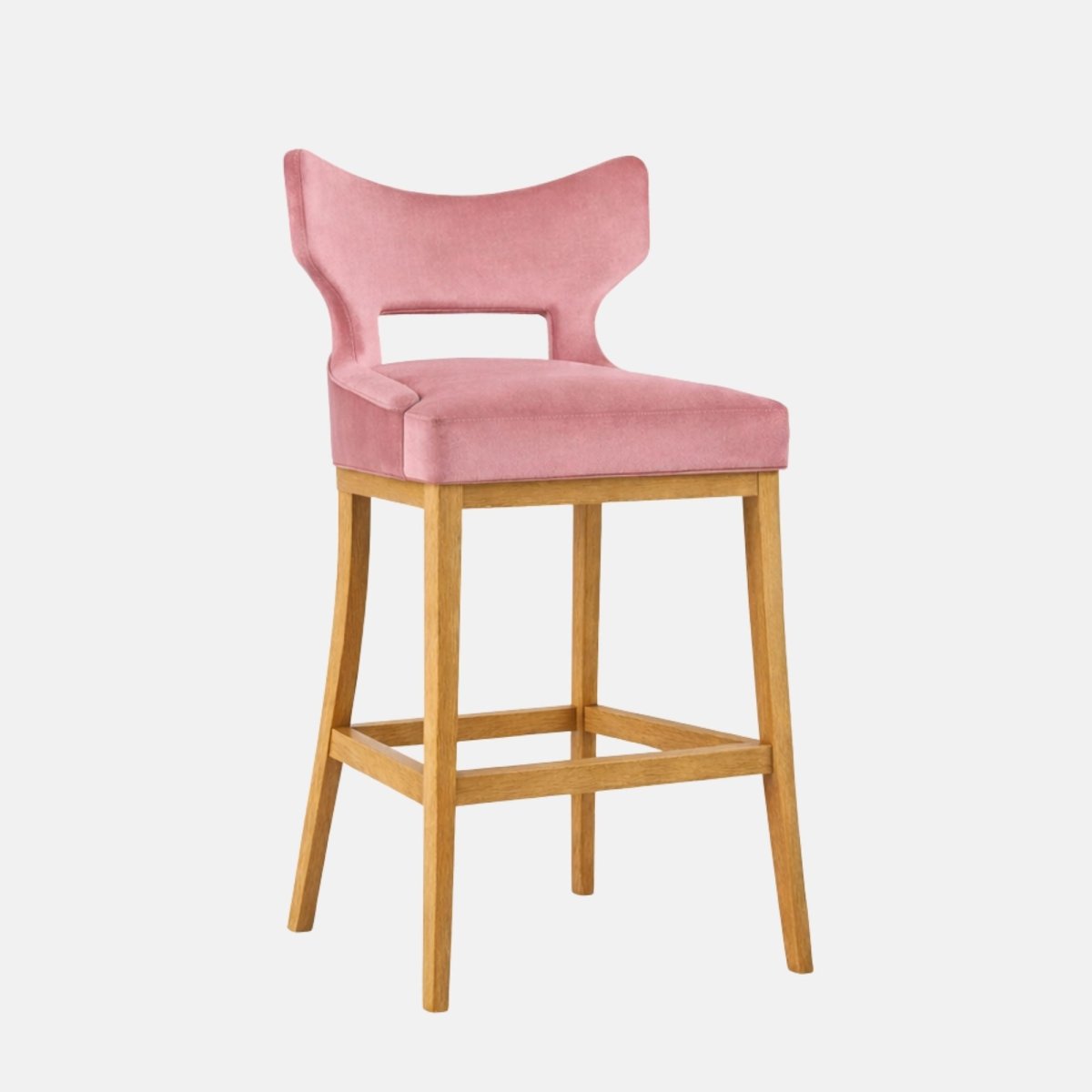 Bar-height stool with blush pink velvet upholstery and a sculptural open-back design, featuring a wide curved backrest with cut-out gap, a thick padded seat, and a light oak wood four-leg frame with square stretchers, shown on a white background.