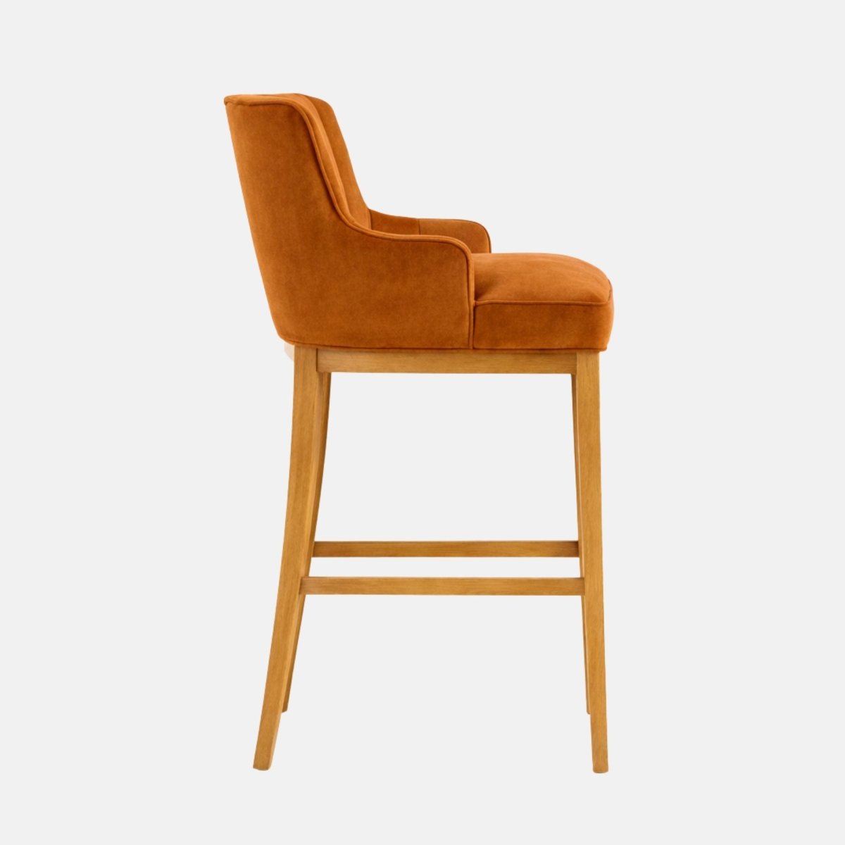 Side view of a rust velvet bar stool with a wraparound curved back and integrated arms, thick cushioned seat, and light oak wooden legs with stretchers, photographed on a white background