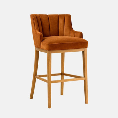 Front view of a rust velvet bar stool with a channel-stitched wraparound back and integrated arms, thick cushioned seat, and light oak wooden legs with square stretchers, on a white background.