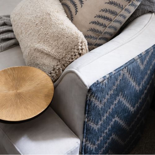 Close up of modern upholstered sofa with decorative throw pillows and gold accent table
