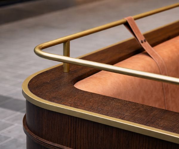 Close-up of a luxury wooden bar counter with brass rail detailing and leather upholstery.