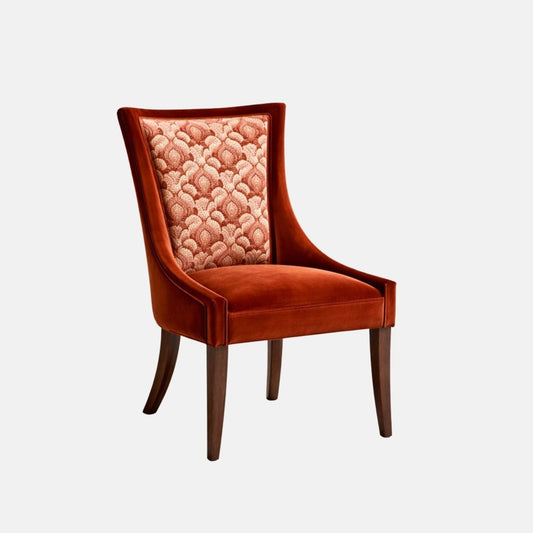 Upholstered accent chair in rust-orange velvet with a patterned fabric panel on the inner backrest, curved arms, cushioned seat, and dark wooden legs, shown against a white background