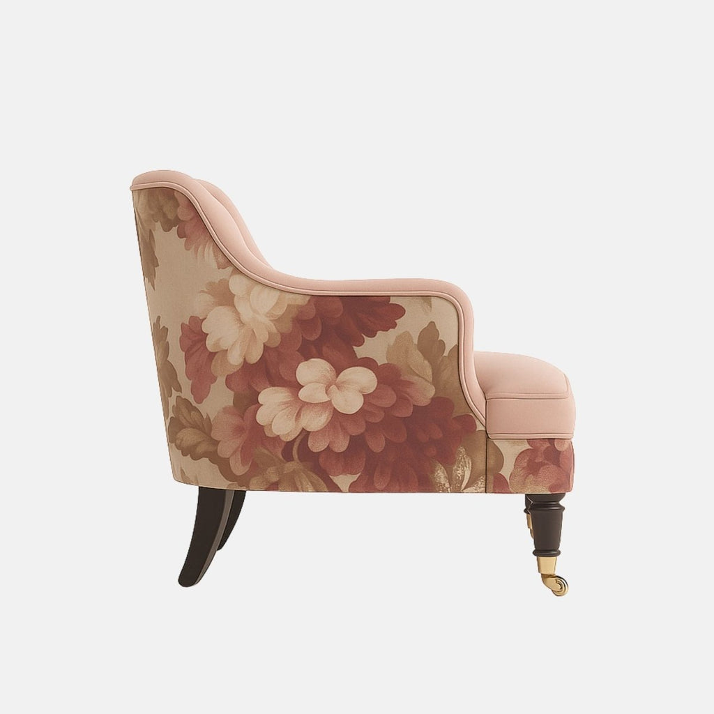 Blush pink lounge chair with curved arms, black legs with brass castors, and floral patterned fabric on the outer back and lower sides