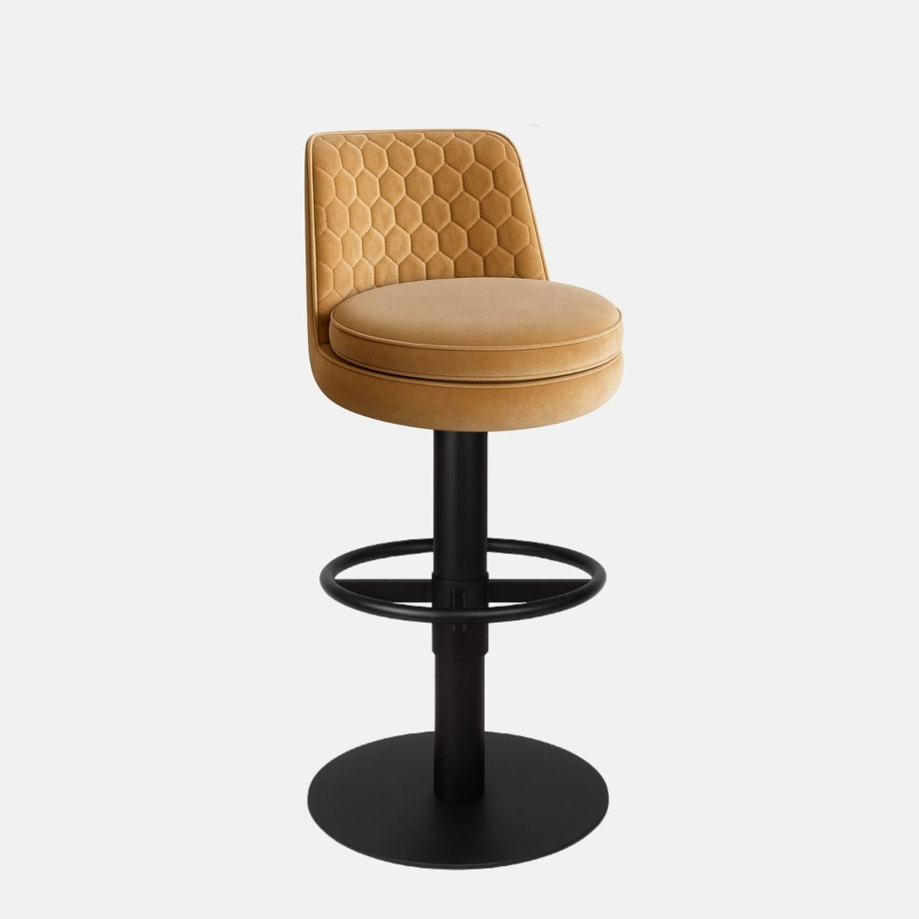 Mustard yellow upholstered bar stool with a hexagonal quilted backrest, round cushioned seat, black circular footrest, and round black metal base on a white background