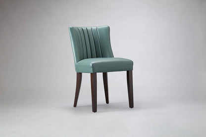 alt="Green dining chair with elegant flute back design, soft leather upholstery, and black legs"