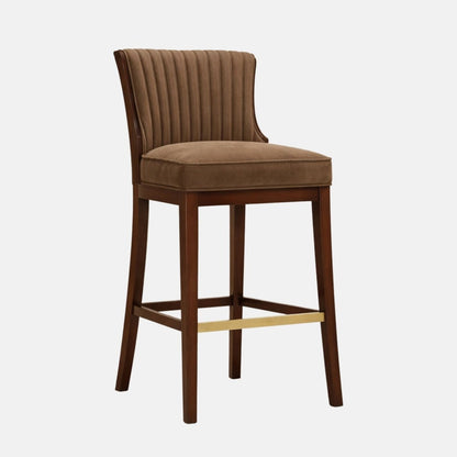 Brown upholstered bar stool with a vertically channel-tufted backrest, padded seat, and dark wooden legs with a brass footrest bar.
