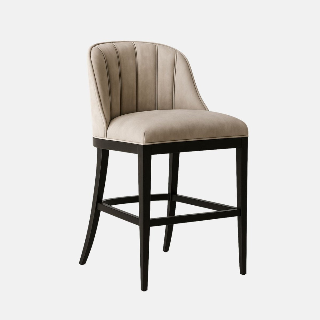 Modern bar stool with a curved backrest and vertical channel stitching, upholstered in light taupe suede fabric. The design features a plush cushioned seat supported by a sleek black wooden frame with a footrest for comfort.