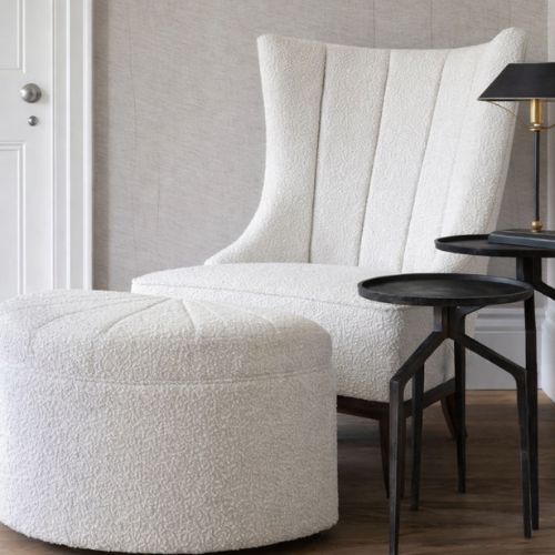 Modern boucle accent chair with matching ottoman and black side tables in minimalist interior