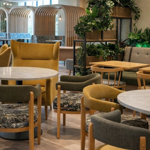 Modern cafe interior with upholstered chairs, round tables and stylish indoor plants