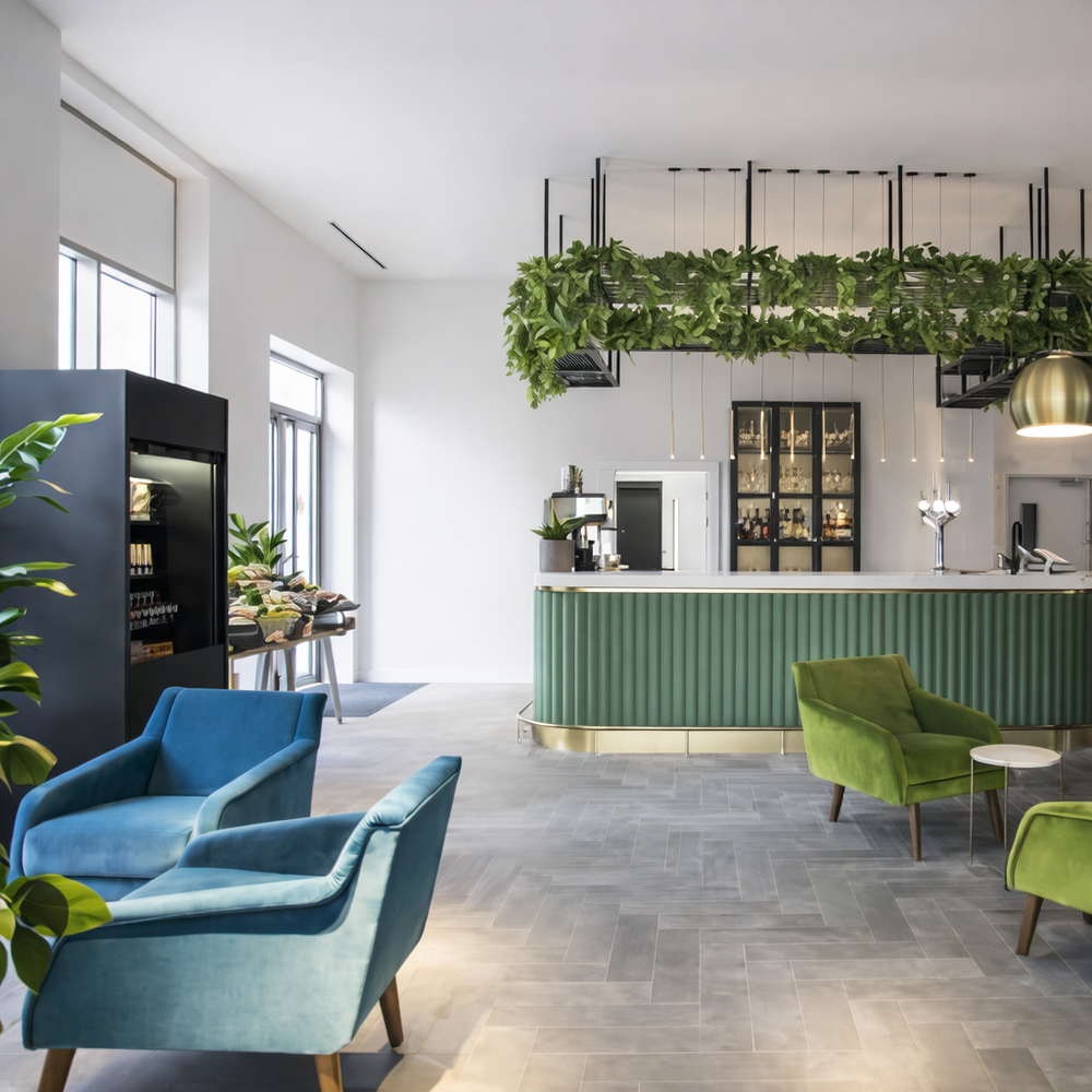 Modern café lounge interior with upholstered armchairs, green bar counter, and indoor plants in a contemporary hospitality space