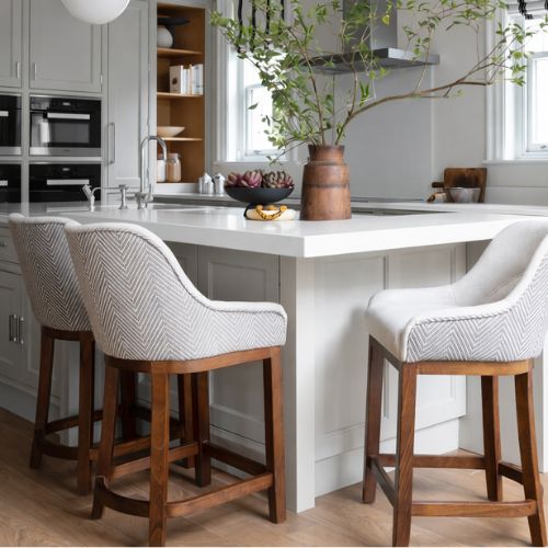 Modern kitchen island with upholstered bar stools and wooden legs in bright contemporary interior
