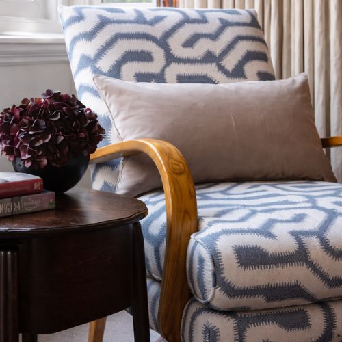 Modern patterned accent chair with decorative pillow and wooden armrest in cozy living room
