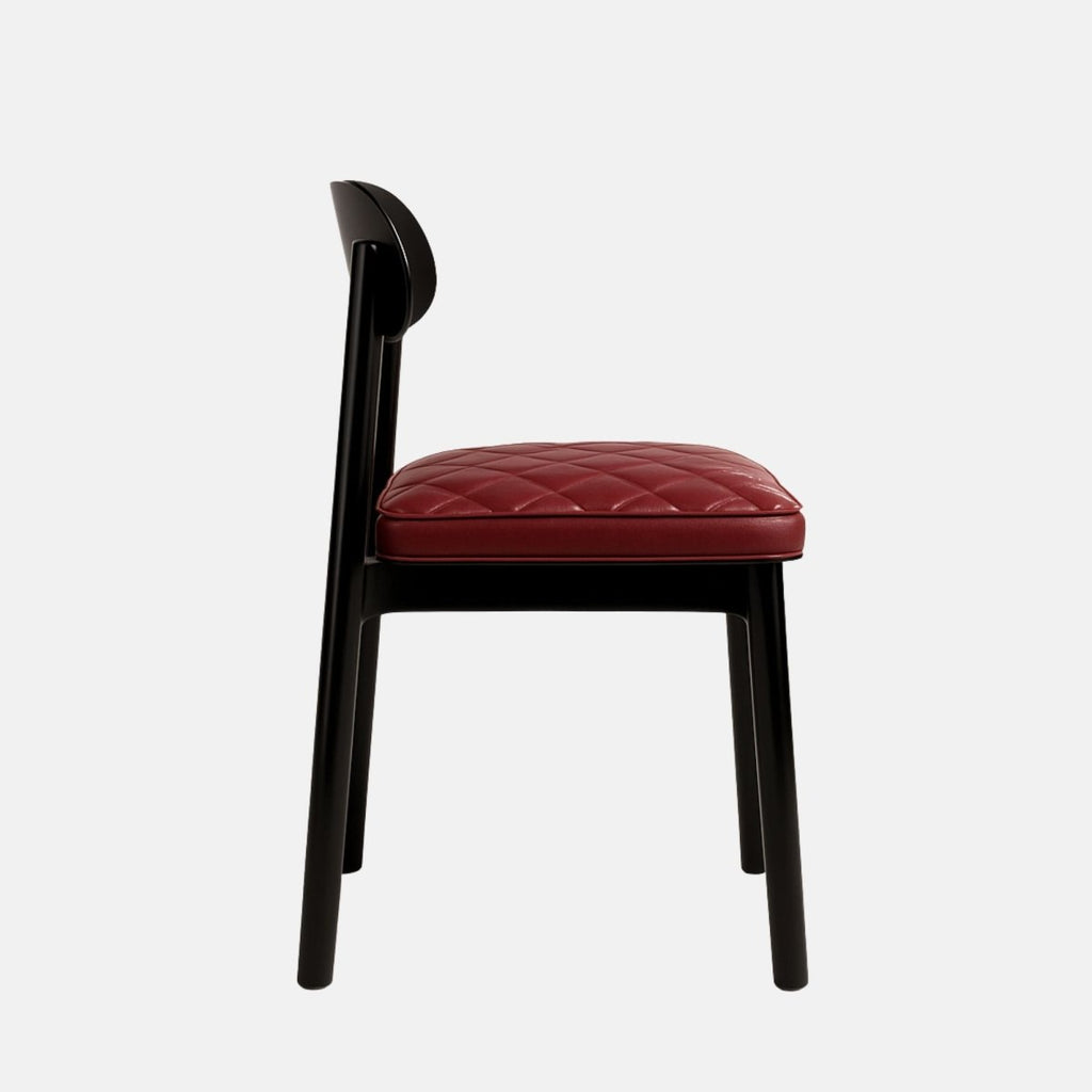 Contemporary dining chair with a black wooden frame and a curved backrest, featuring a quilted burgundy leather seat cushion and minimalist design, set against a light grey background