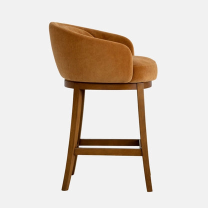 Side profile of a caramel-brown upholstered bar stool with a rounded tub-style back and curved arms, padded seat, and dark wooden legs with a horizontal footrest, photographed on a white background.