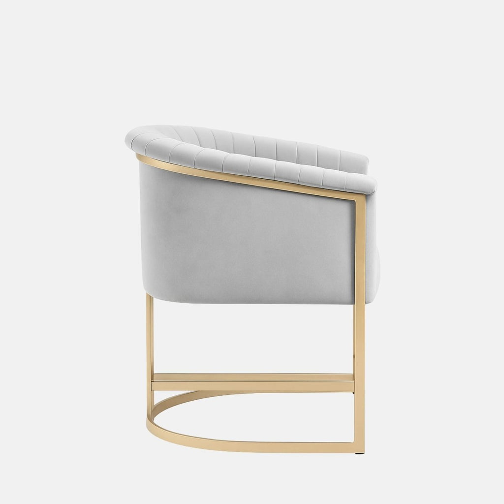 Light grey velvet upholstered chair with vertical channel stitching, curved backrest, and a gold metal frame base.