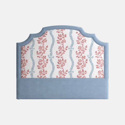 Upholstered headboard with a scalloped blue frame and floral patterned fabric in soft red and blue tones, set against a plain background.