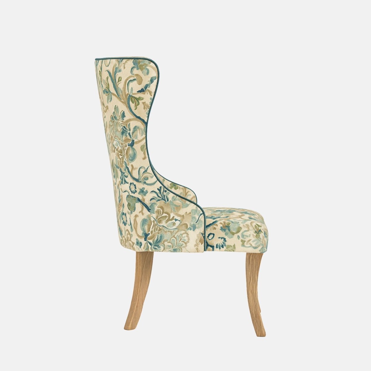 Side view of a high-back wing dining chair upholstered in cream floral fabric with teal piping and light oak wooden legs, photographed on a white background.
