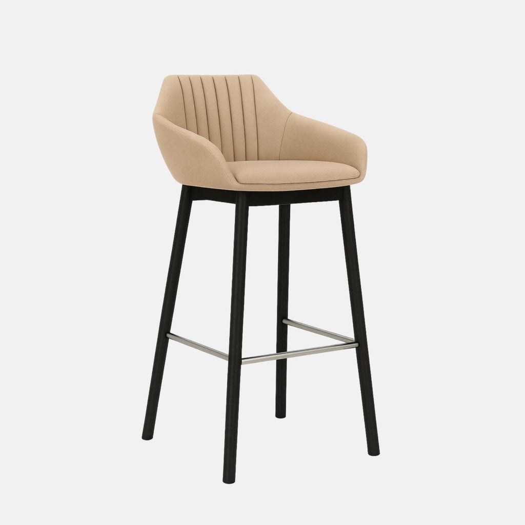 Beige upholstered bar stool with a curved backrest and armrests, subtle vertical stitching, black wooden legs, and a metal footrest.