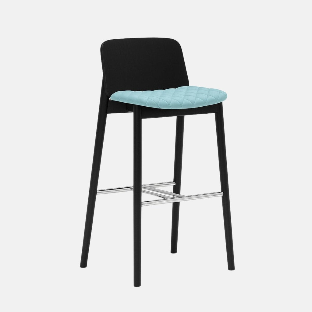 Modern bar stool with a black wooden frame, low curved backrest, light blue quilted seat, and metal footrest.
