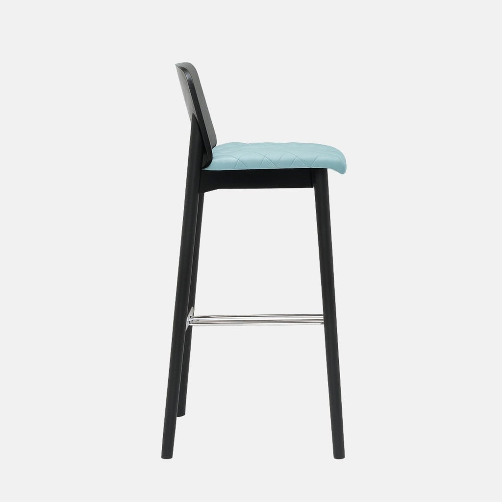 Modern bar stool with a black wooden frame, low curved backrest, light blue quilted seat, and metal footrest.