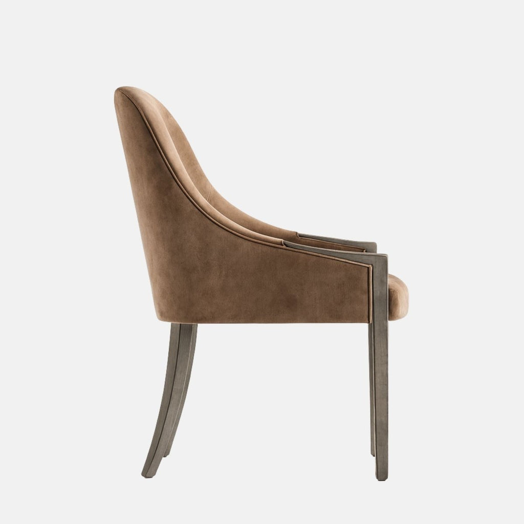 Upholstered dining chair in warm taupe-brown fabric with a rounded backrest, subtle arm supports, cushioned seat, and dark wooden legs, shown on a white background