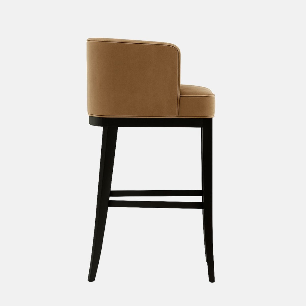 Upholstered bar stool with a curved camel-colored seat, black tapered legs, and a gold metal footrest.