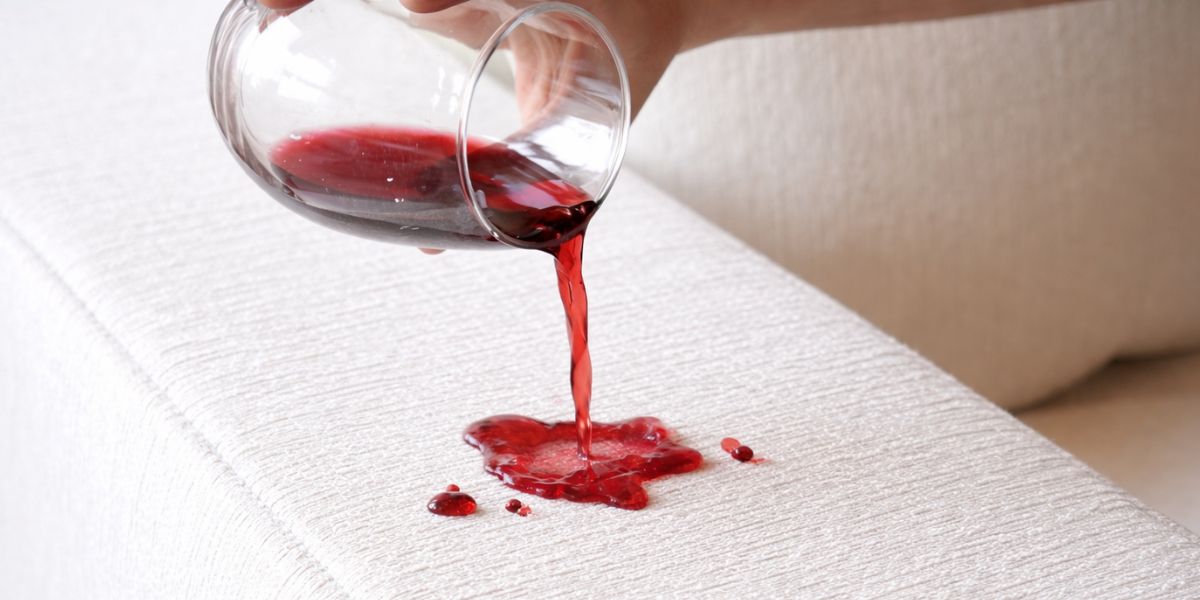 Red wine spilling onto light upholstered sofa fabric