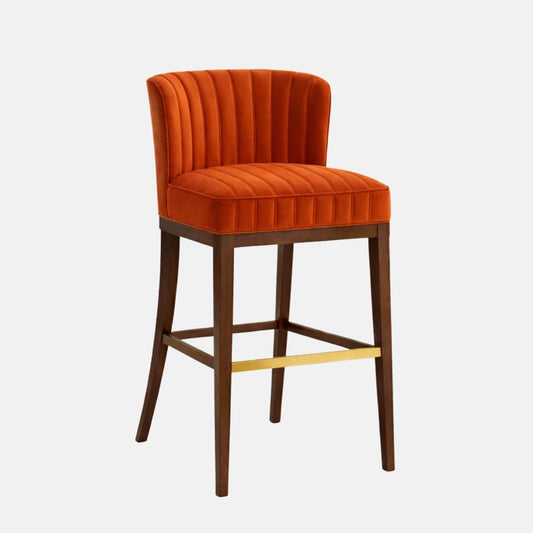 Burnt orange velvet bar stool with curved channel-tufted back and ribbed seat, on dark wood legs with square stretchers and a brass front footrest, isolated on a white background.