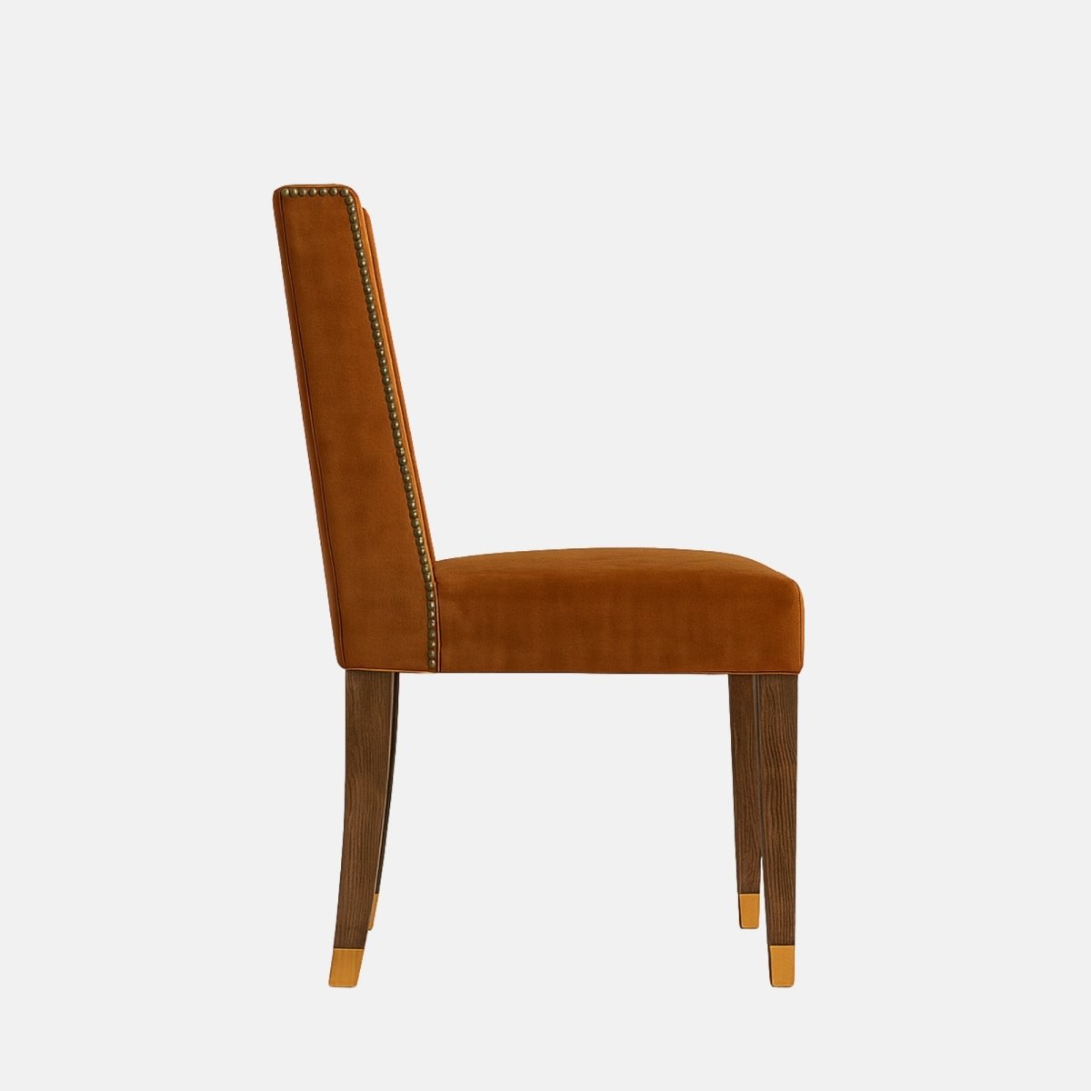 Side view of an armless dining chair upholstered in burnt orange velvet with nailhead trim along the back, dark wooden legs with brass caps, photographed on a white background.
