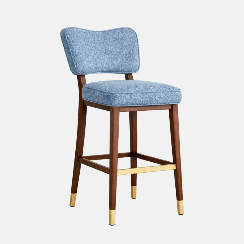 Blue patterned upholstered bar stool with a curved backrest, thick seat cushion, dark wooden legs, and brass footrest and leg caps.