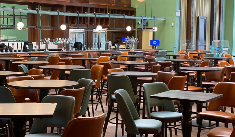 Restaurant dining area with bar counter, wooden tables, and colourful upholstered chairs. 